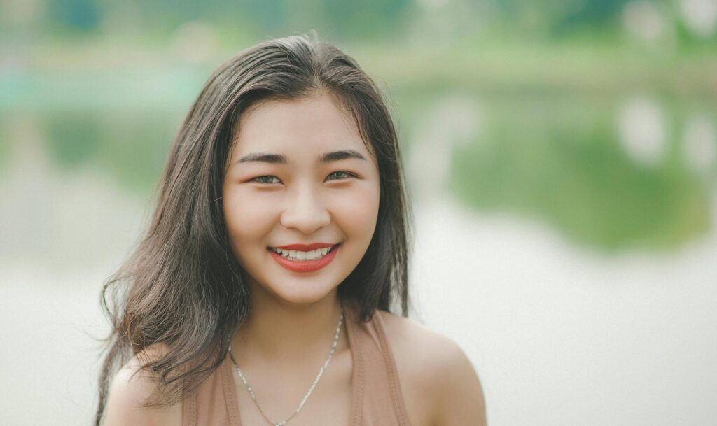 A cheerful young woman smiles brightly in an outdoor setting by the lake.